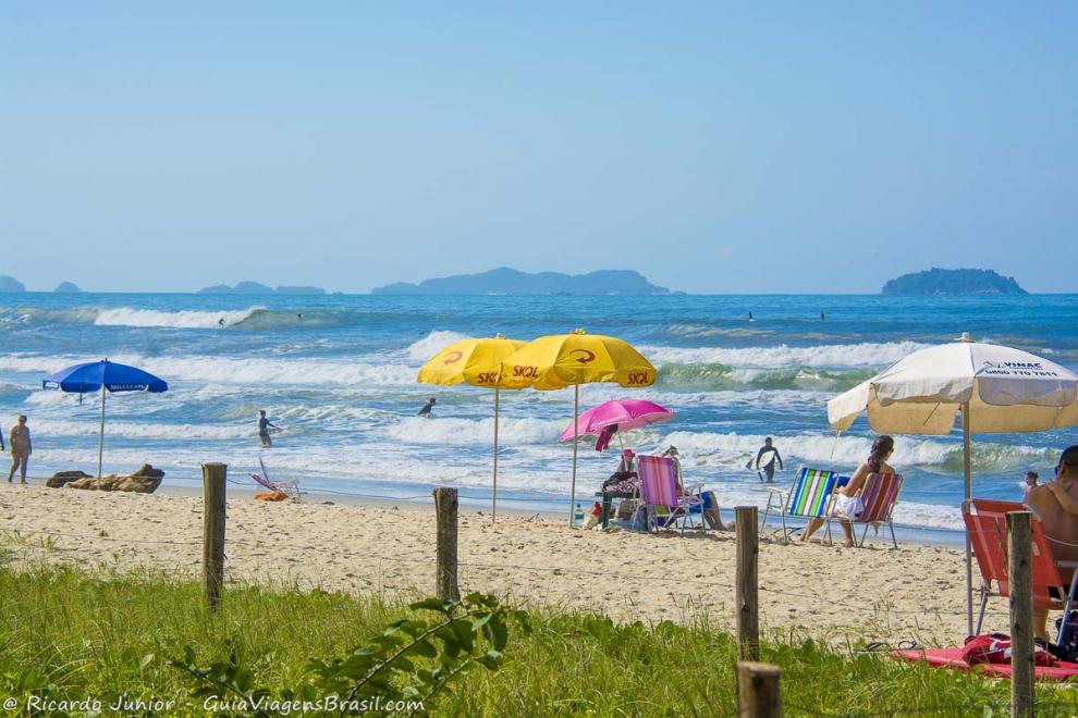 Imagem de vários guarda sol e surfistas nas ondas da Praia de Itamambuca.